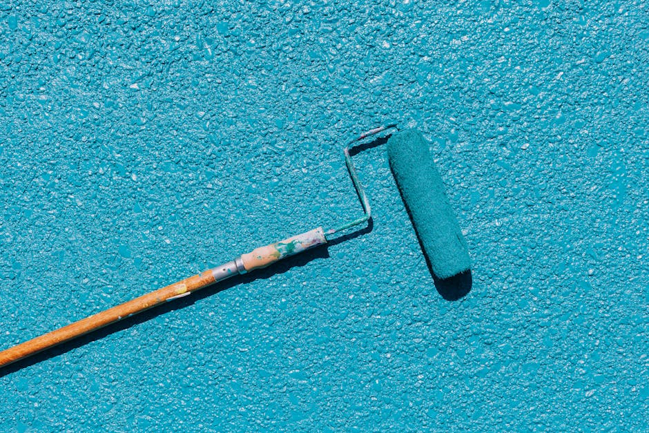 A close-up of a blue paint roller applying paint on a textured wall surface, captured in bright sunlight.