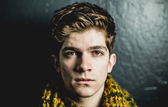 Close-up portrait of a young adult male with a serious expression against a dark textured wall.
